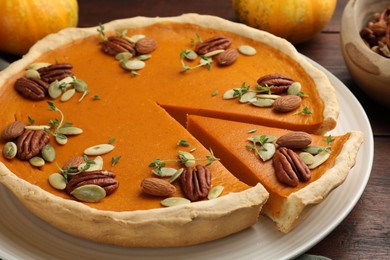 Photo of Tasty homemade pumpkin pie with nuts and seeds on wooden table, closeup