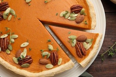 Tasty homemade pumpkin pie with nuts and seeds on wooden table, top view