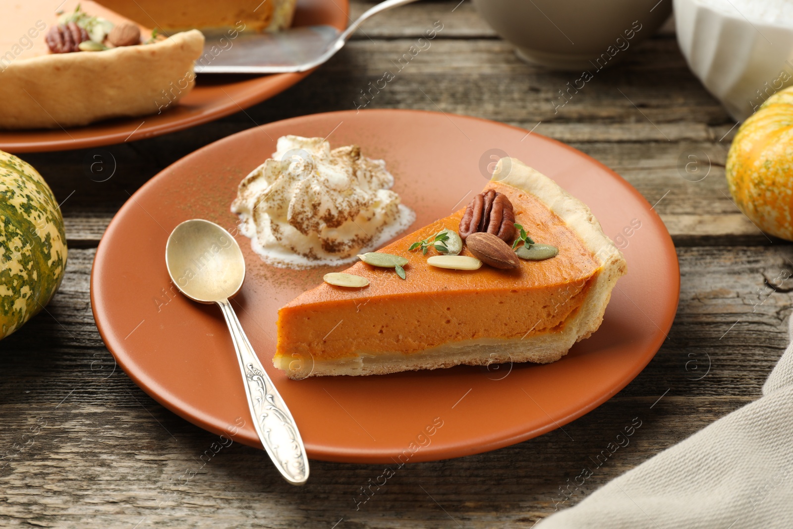 Photo of Piece of tasty homemade pumpkin pie with whipped cream, seeds and nuts on wooden table, closeup