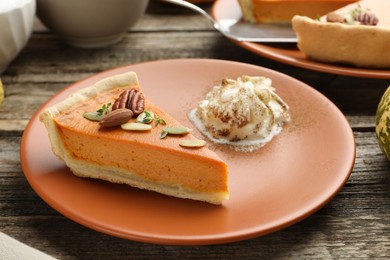 Piece of tasty homemade pumpkin pie with whipped cream, seeds and nuts on wooden table, closeup