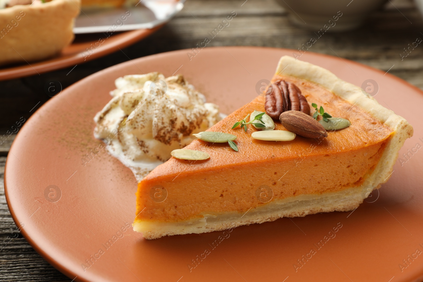 Photo of Piece of tasty homemade pumpkin pie with whipped cream, seeds and nuts on table, closeup