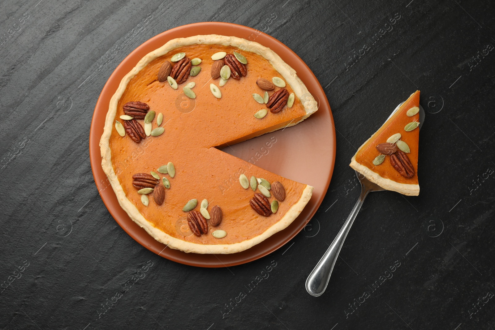 Photo of Tasty homemade pumpkin pie and server on black table, top view