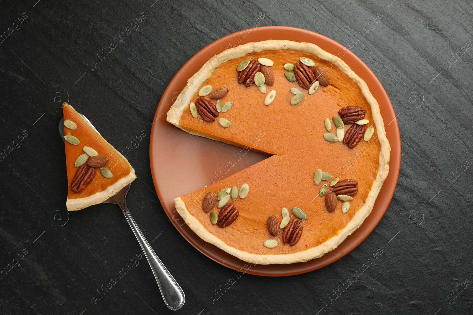 Photo of Tasty homemade pumpkin pie and server on black table, top view