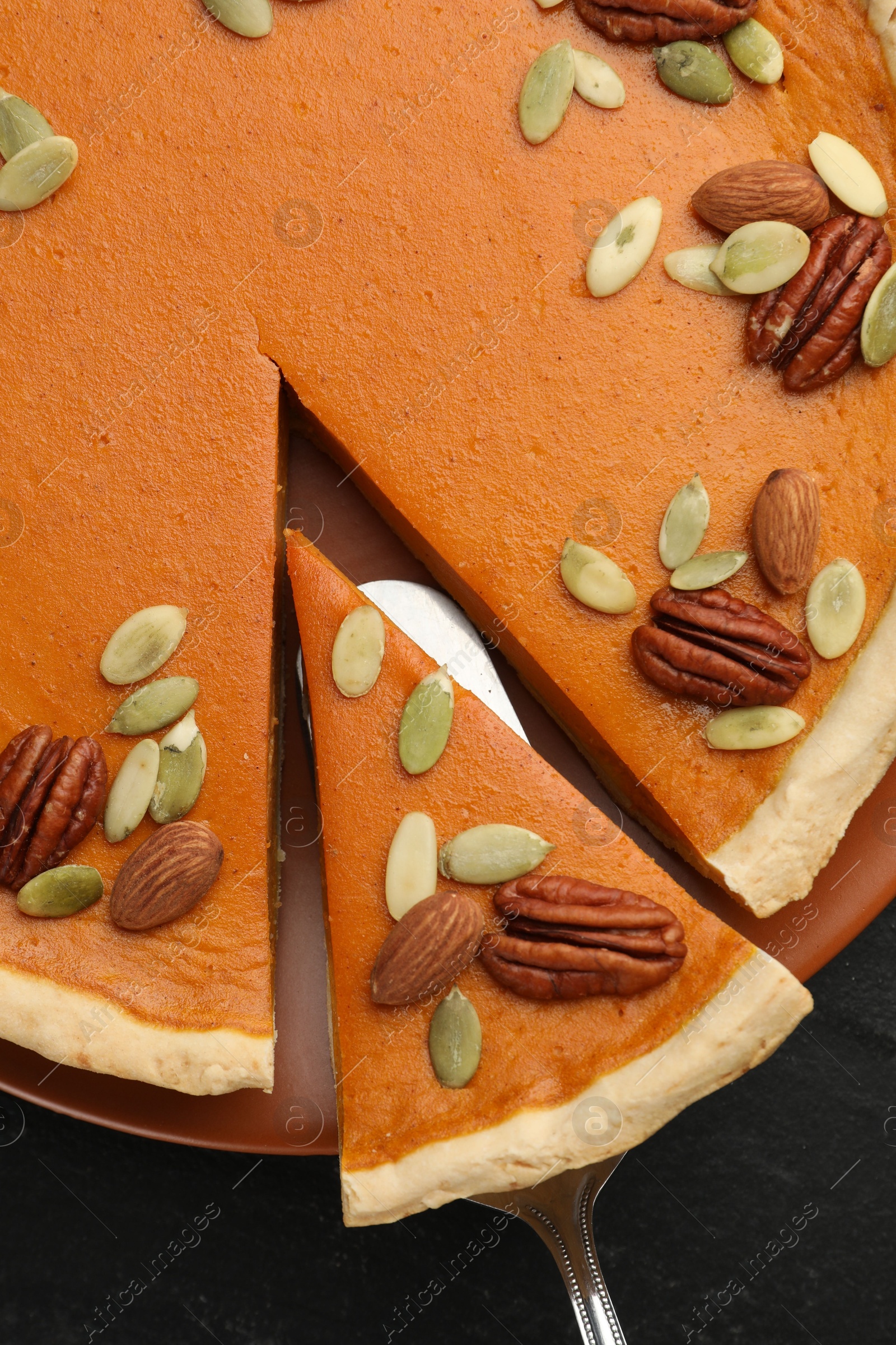 Photo of Taking piece of tasty homemade pumpkin pie at black table, top view