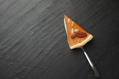 Photo of Piece of tasty homemade pumpkin pie with seeds, nuts and server on black table, top view. Space for text