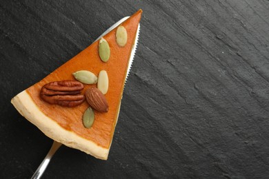 Photo of Piece of tasty homemade pumpkin pie with seeds, nuts and server on black table, top view. Space for text