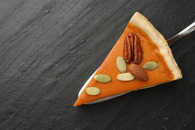 Piece of tasty homemade pumpkin pie with seeds, nuts and server on black table, top view. Space for text