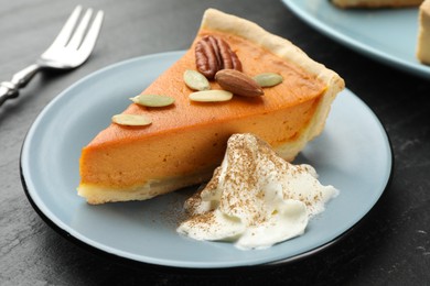 Photo of Piece of tasty homemade pumpkin pie with whipped cream, seeds and nuts on black table, closeup