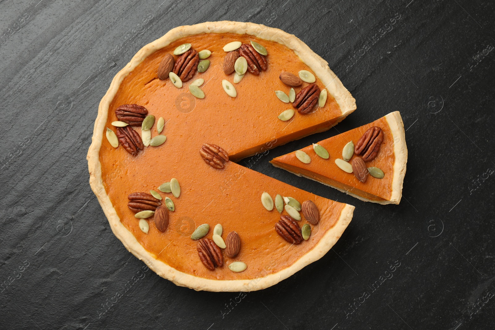 Photo of Tasty homemade pumpkin pie with seeds and nuts on black table, top view