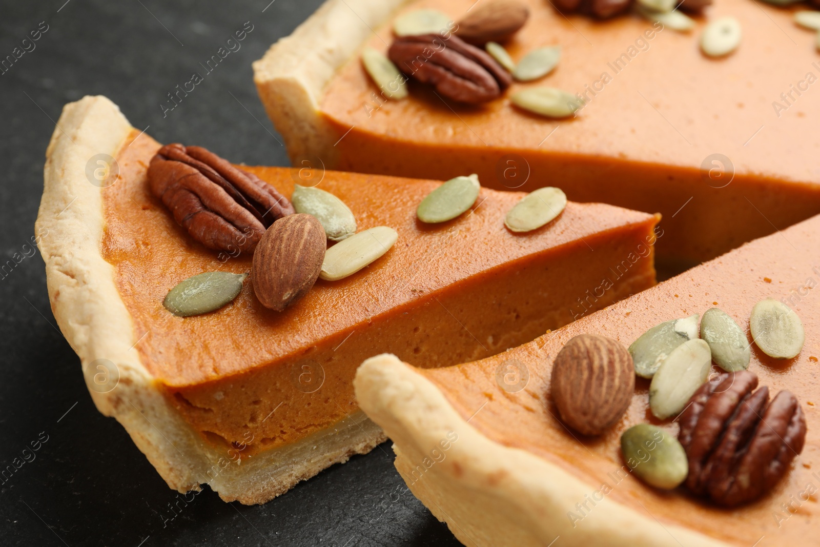 Photo of Pieces of tasty homemade pumpkin pie with seeds and nuts on black table, closeup