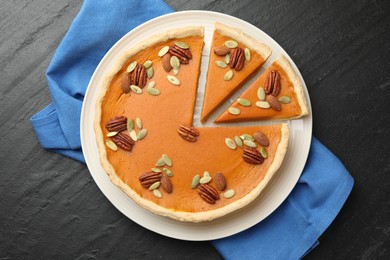 Photo of Tasty homemade pumpkin pie with seeds and nuts on black table, top view