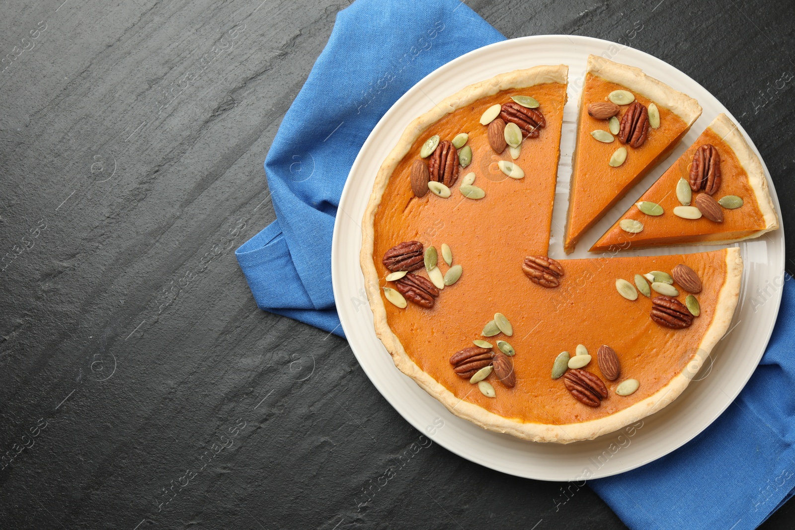 Photo of Tasty homemade pumpkin pie with seeds and nuts on black table, top view. Space for text