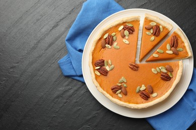 Tasty homemade pumpkin pie with seeds and nuts on black table, top view. Space for text