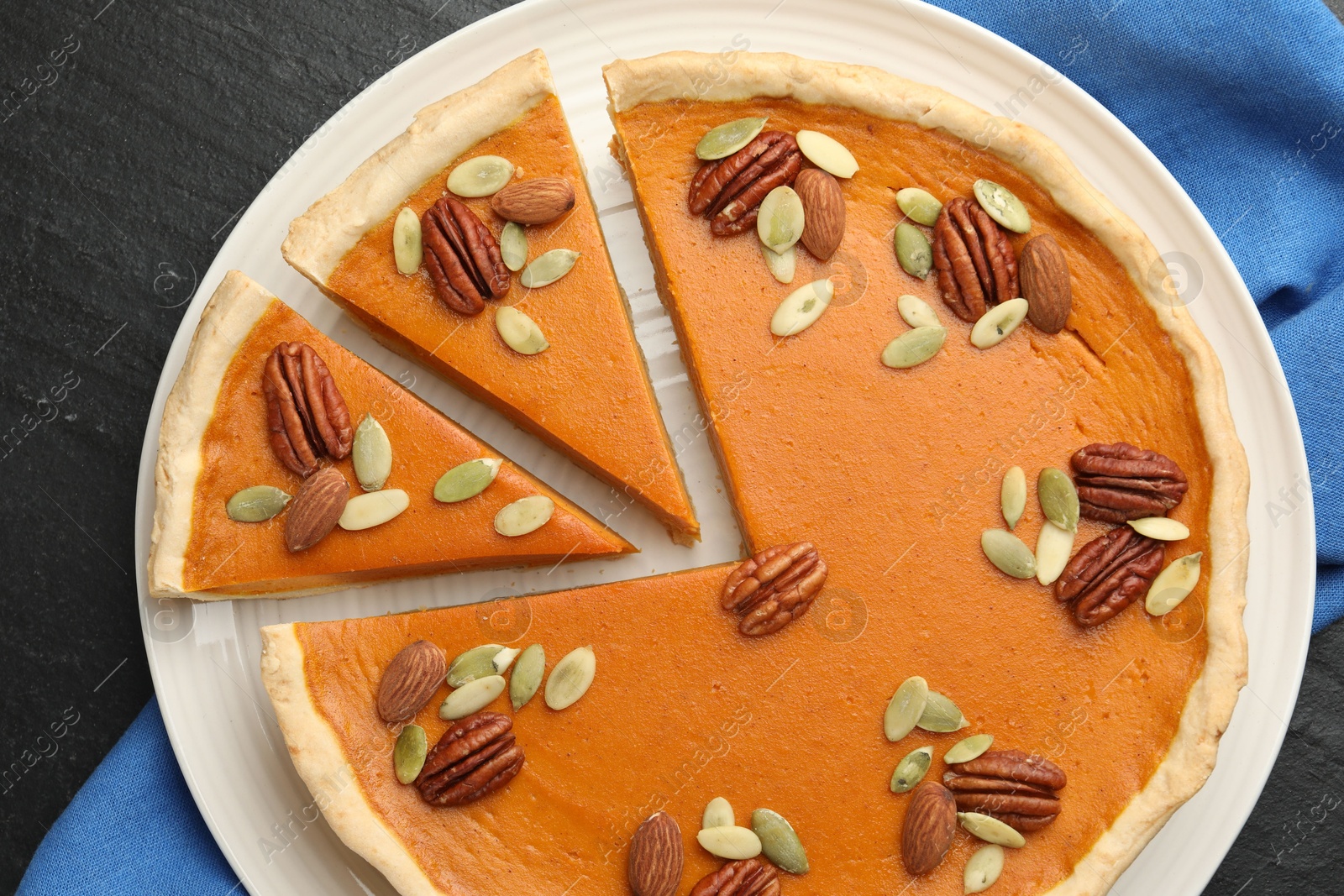 Photo of Tasty homemade pumpkin pie with seeds and nuts on black table, top view