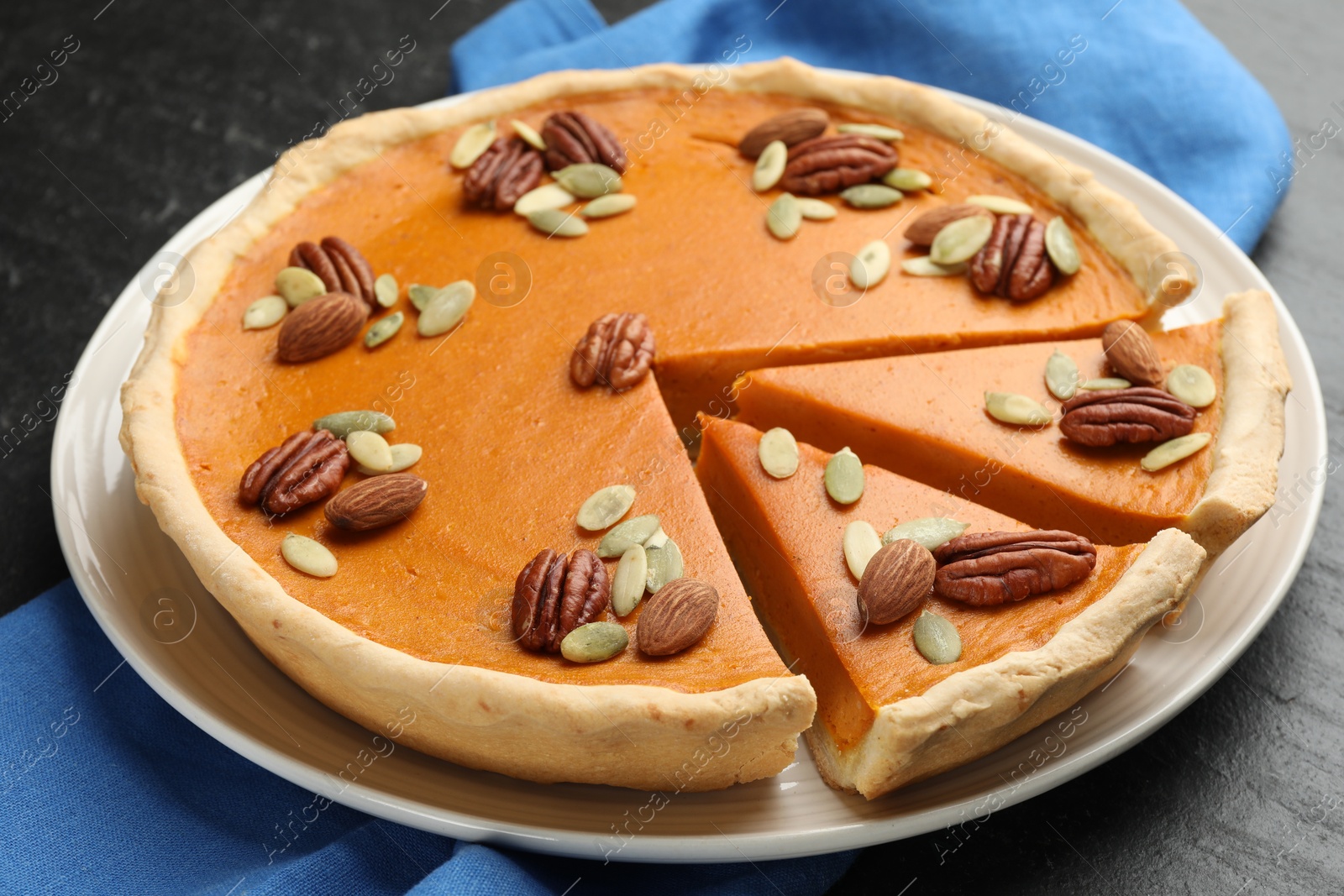 Photo of Tasty homemade pumpkin pie with seeds and nuts on black table, closeup