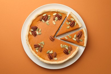 Photo of Tasty homemade pumpkin pie with seeds and nuts on orange background, top view