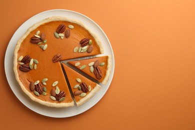 Photo of Tasty homemade pumpkin pie with seeds and nuts on orange background, top view. Space for text