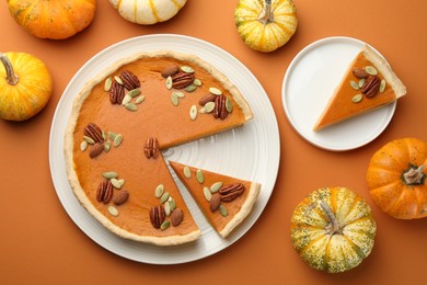 Tasty homemade pumpkin pie and fresh pumpkins on orange background, top view