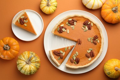 Tasty homemade pumpkin pie and fresh pumpkins on orange background, top view