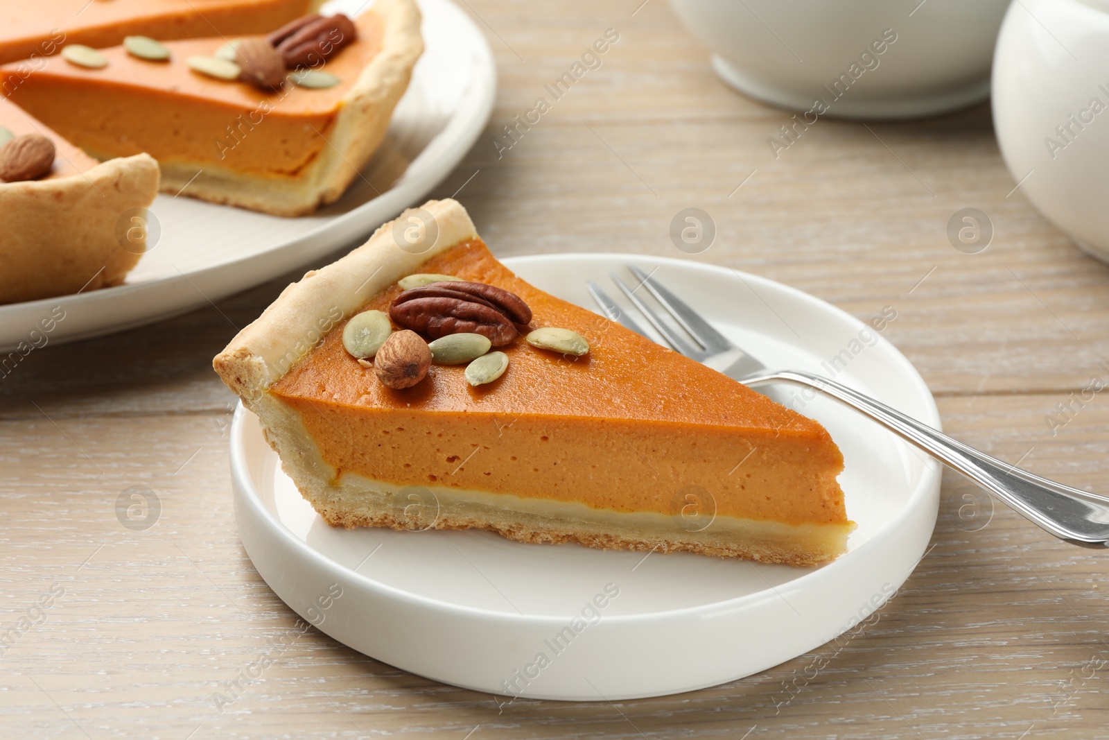 Photo of Piece of tasty homemade pumpkin pie with seeds and nuts on wooden table, closeup