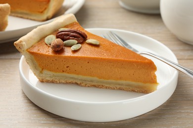 Piece of tasty homemade pumpkin pie with seeds and nuts on wooden table, closeup