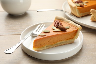 Photo of Piece of tasty homemade pumpkin pie with seeds and nuts on wooden table, closeup