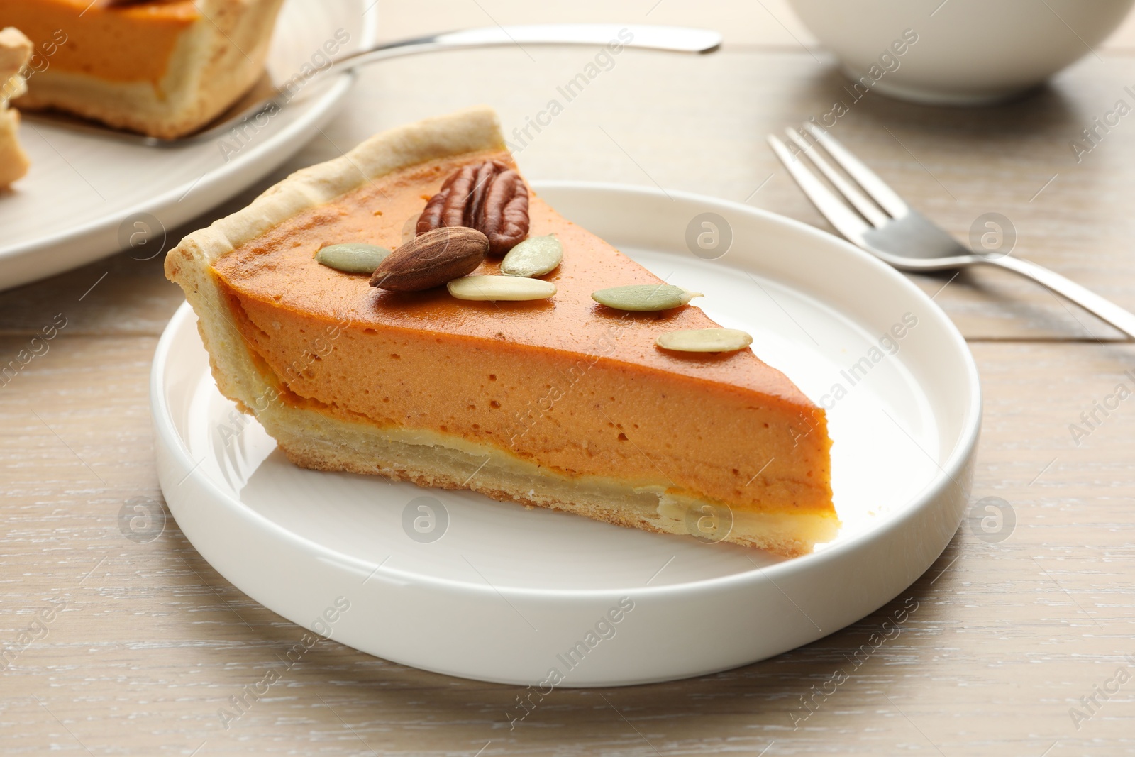 Photo of Piece of tasty homemade pumpkin pie with seeds and nuts on wooden table, closeup