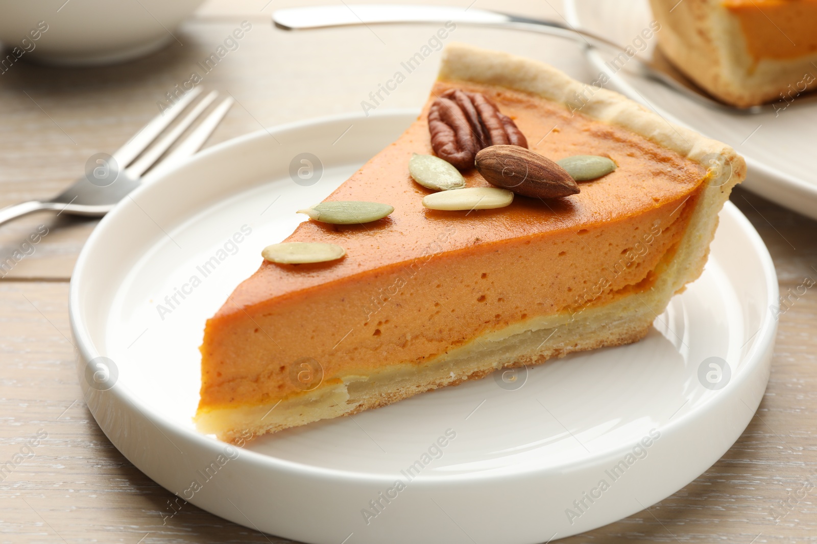 Photo of Piece of tasty homemade pumpkin pie with seeds and nuts on wooden table, closeup