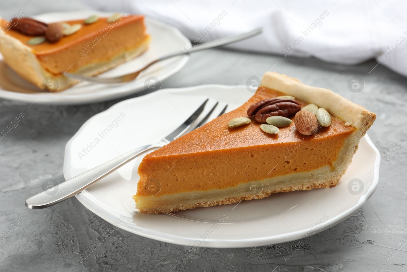 Photo of Pieces of tasty homemade pumpkin pie with seeds and nuts on grey table, closeup