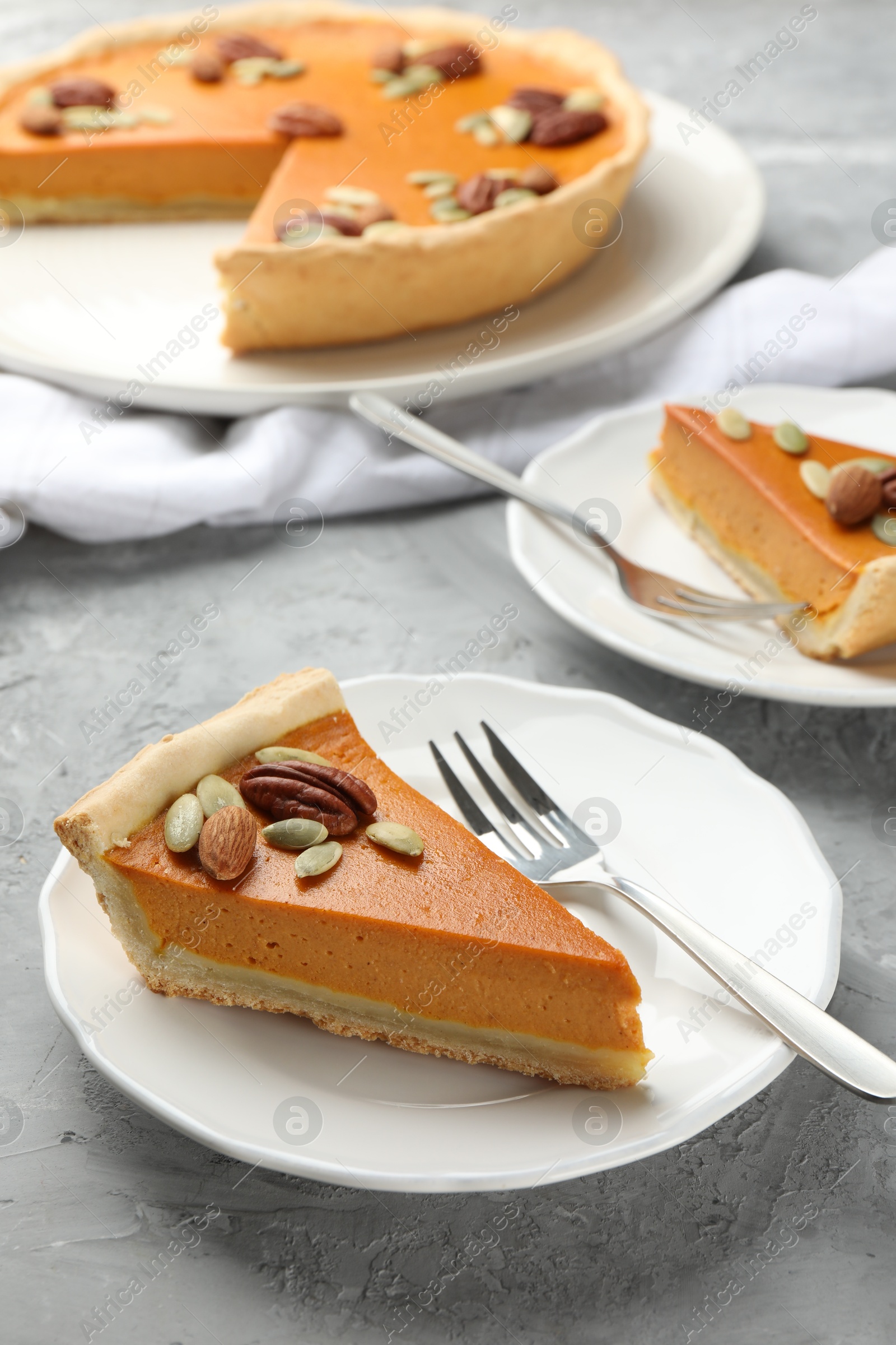 Photo of Pieces of tasty homemade pumpkin pie with seeds and nuts on grey table