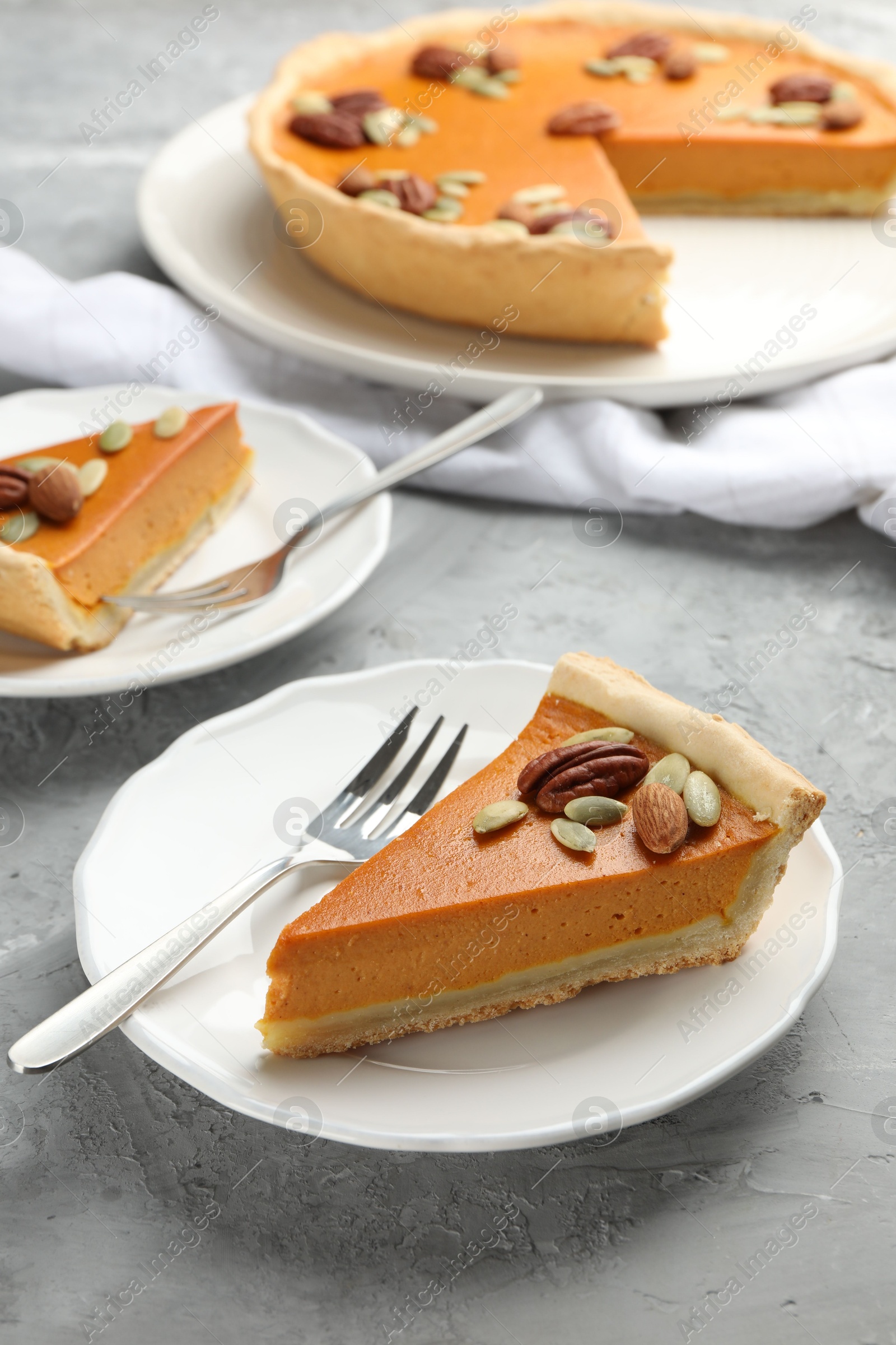 Photo of Pieces of tasty homemade pumpkin pie with seeds and nuts on grey table