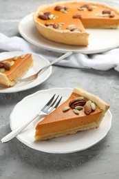 Pieces of tasty homemade pumpkin pie with seeds and nuts on grey table