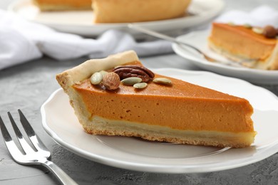 Photo of Piece of tasty homemade pumpkin pie with seeds and nuts on grey table, closeup