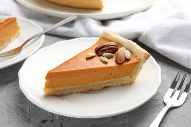 Photo of Piece of tasty homemade pumpkin pie with seeds and nuts on grey table, closeup