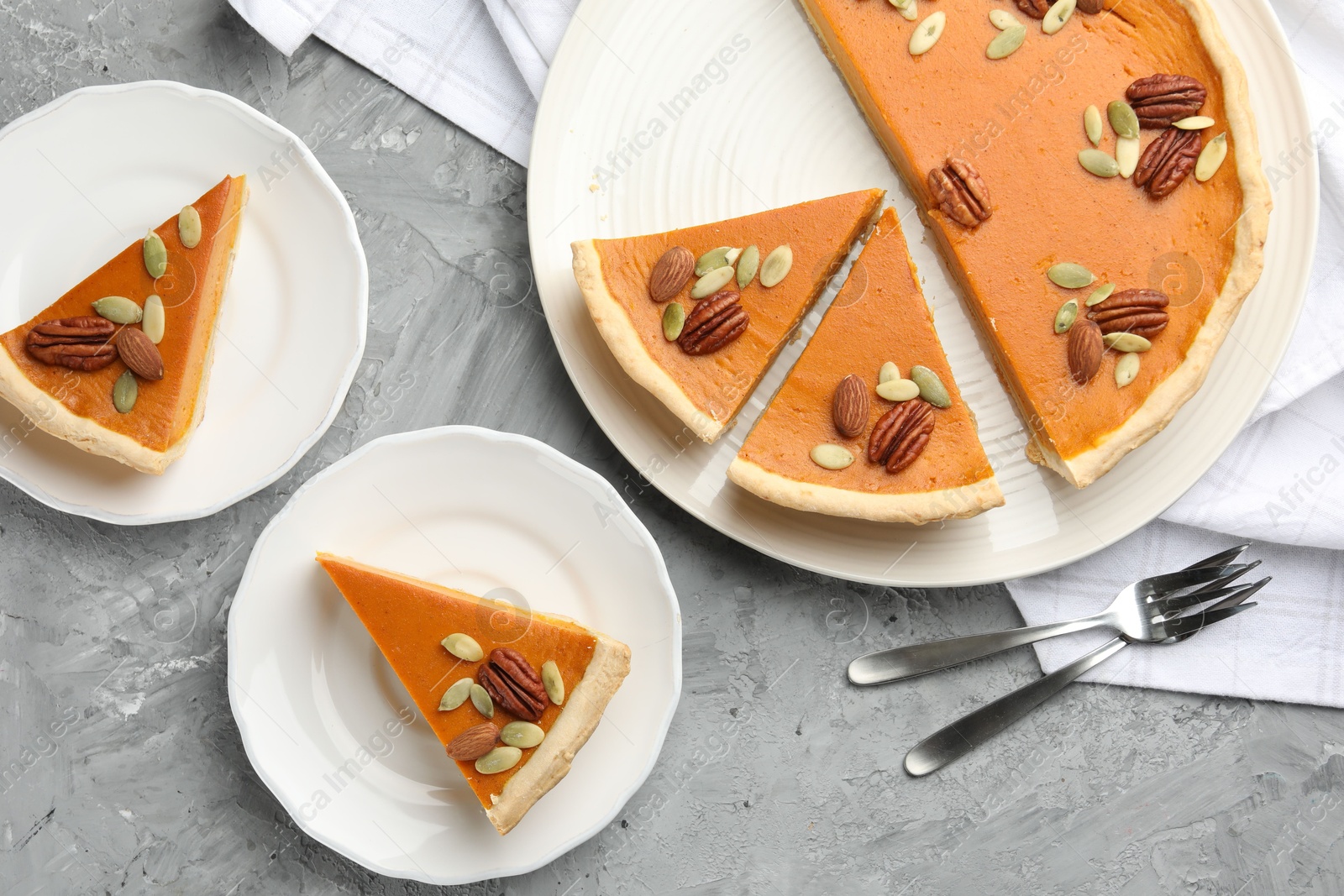 Photo of Pieces of tasty homemade pumpkin pie with seeds and nuts on grey table, top view