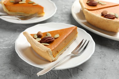 Photo of Pieces of tasty homemade pumpkin pie with seeds and nuts on grey table, closeup