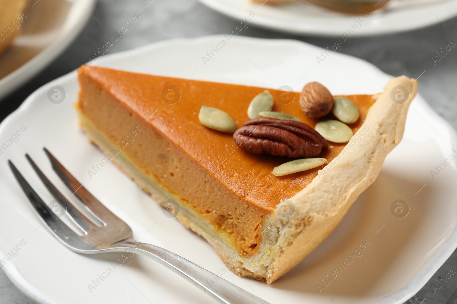 Photo of Piece of tasty homemade pumpkin pie with seeds and nuts on table, closeup