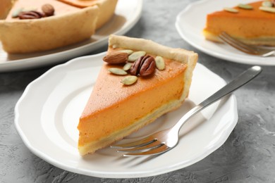 Photo of Pieces of tasty homemade pumpkin pie with seeds and nuts on grey table, closeup