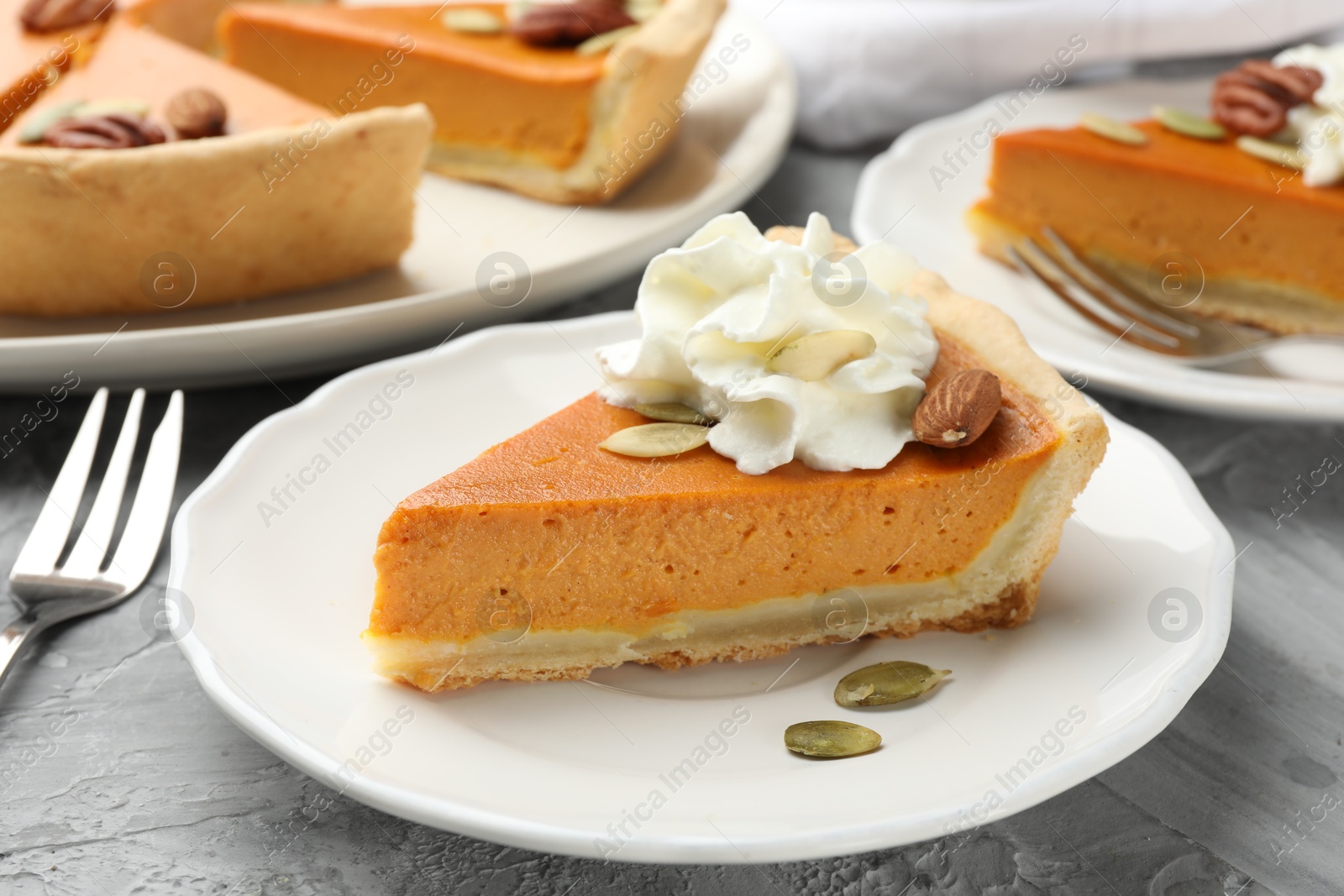 Photo of Pieces of tasty homemade pumpkin pie with whipped cream, seeds and nuts on grey table, closeup