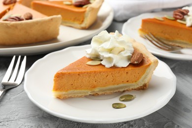 Pieces of tasty homemade pumpkin pie with whipped cream, seeds and nuts on grey table, closeup