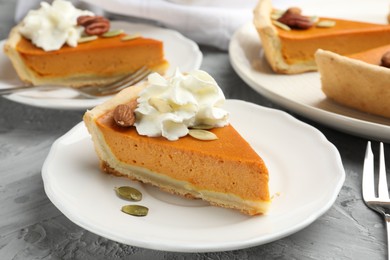 Photo of Pieces of tasty homemade pumpkin pie with whipped cream, seeds and nuts on grey table, closeup