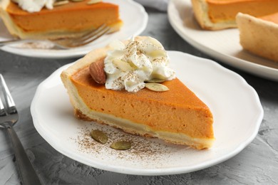 Photo of Piece of tasty homemade pumpkin pie with whipped cream, seeds and almond on grey table, closeup