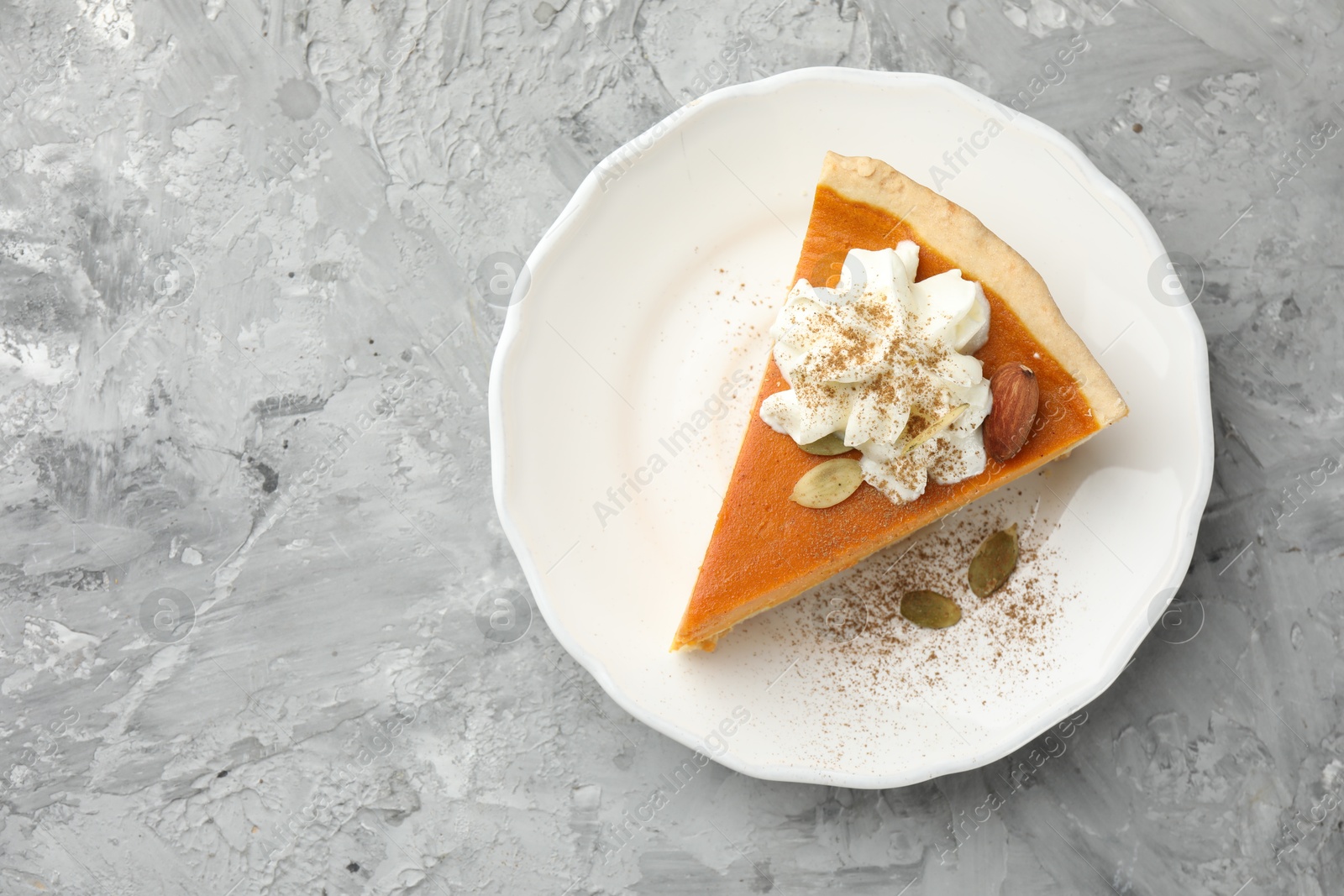 Photo of Piece of tasty homemade pumpkin pie with whipped cream, seeds and almond on grey table, top view. Space for text