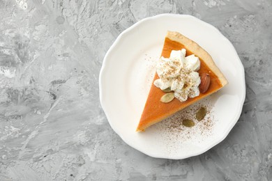 Piece of tasty homemade pumpkin pie with whipped cream, seeds and almond on grey table, top view. Space for text