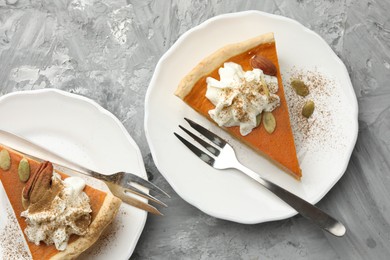 Photo of Pieces of tasty homemade pumpkin pie with whipped cream and seeds on grey table, top view