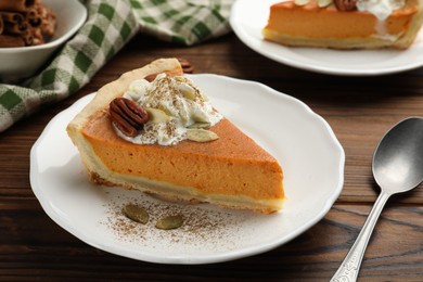 Piece of tasty homemade pumpkin pie with whipped cream, seeds and pecan nut on wooden table, closeup