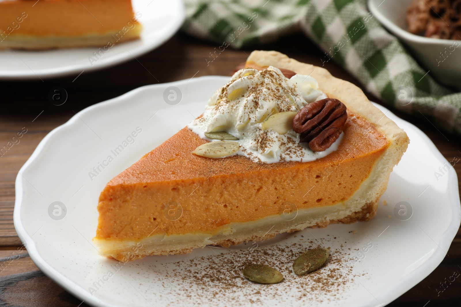 Photo of Piece of tasty homemade pumpkin pie with whipped cream, seeds and pecan nut on table, closeup