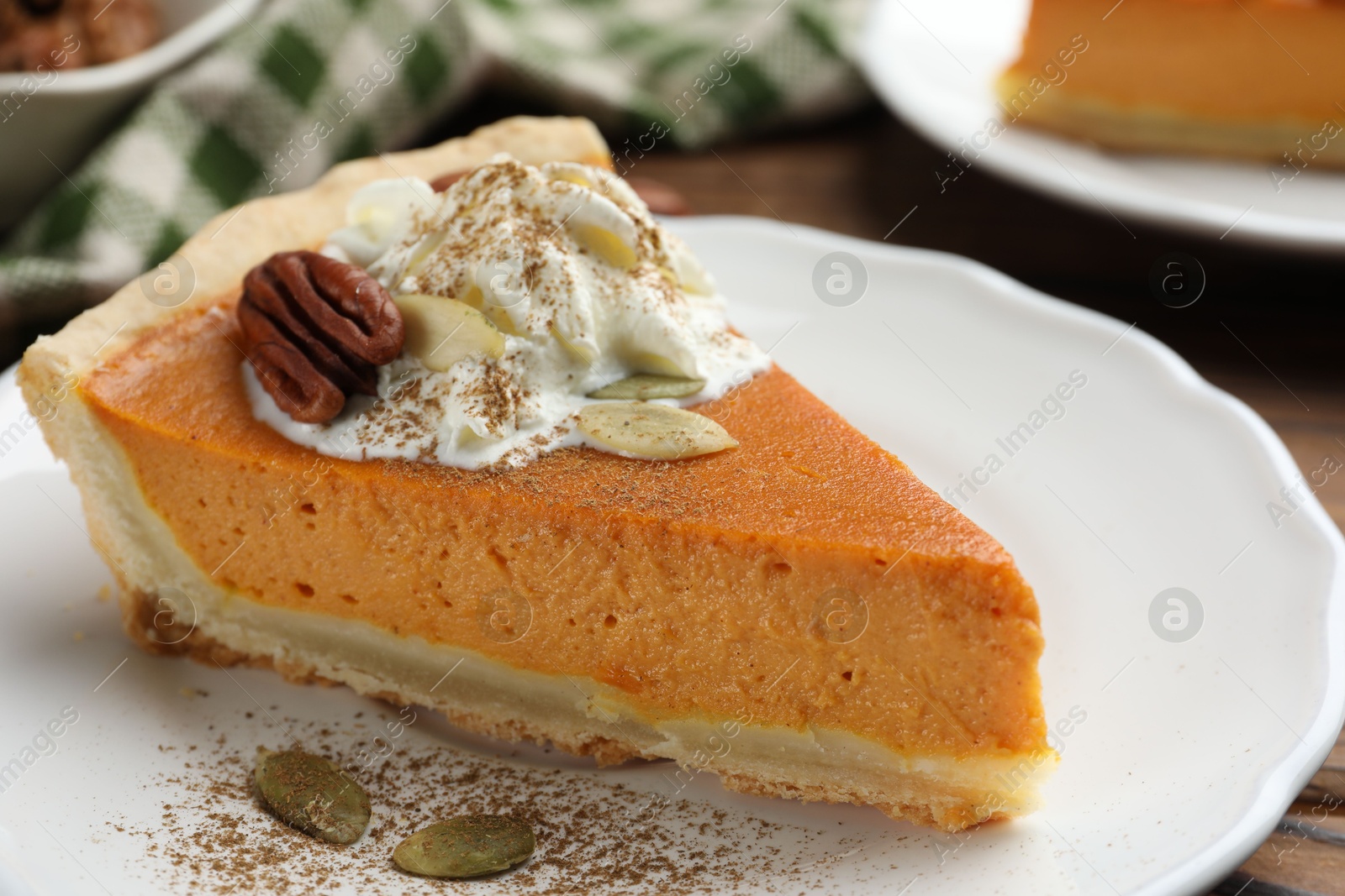 Photo of Piece of tasty homemade pumpkin pie with whipped cream, seeds and pecan nut on table, closeup