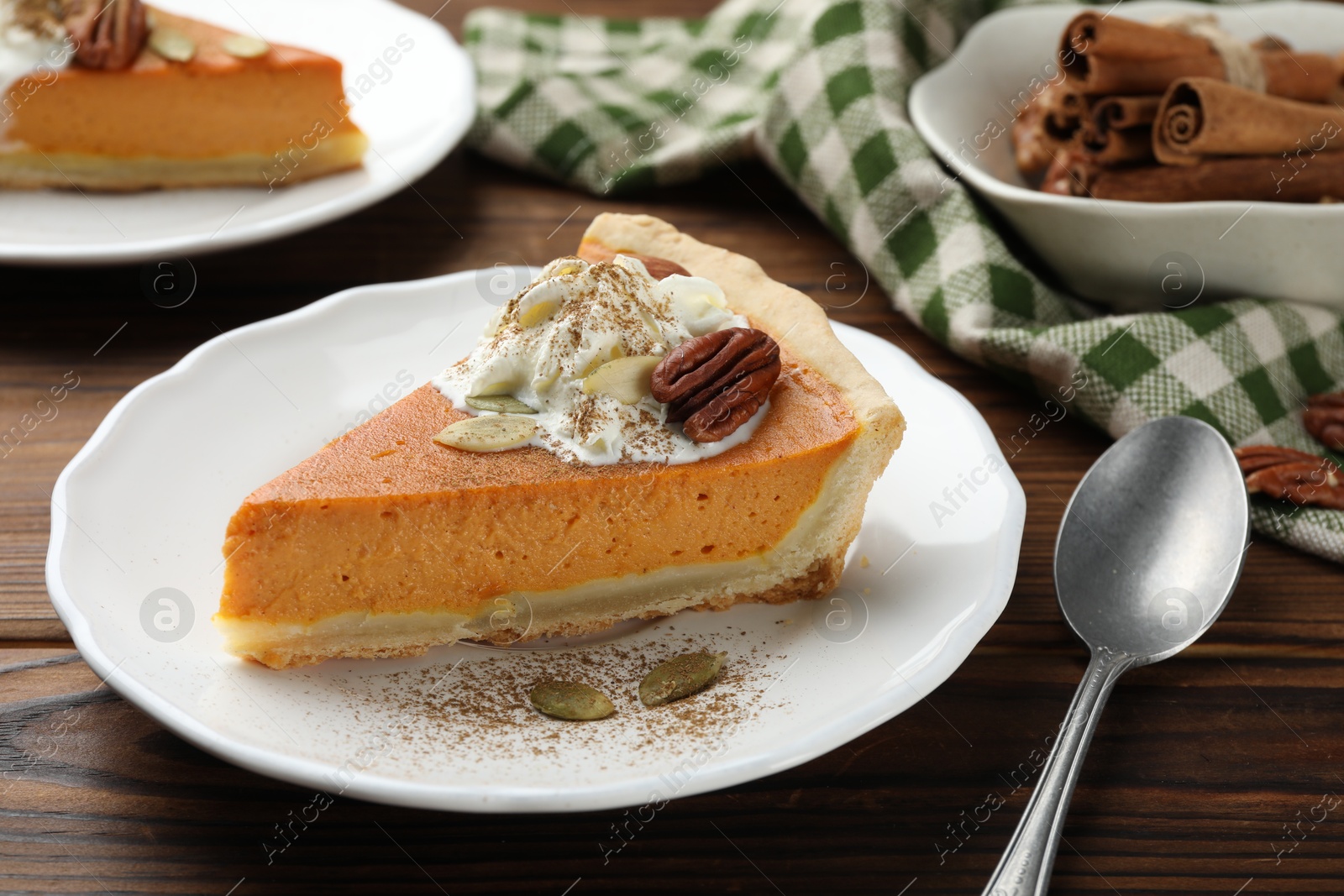 Photo of Piece of tasty homemade pumpkin pie with whipped cream, seeds and pecan nut on wooden table, closeup