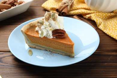 Piece of tasty homemade pumpkin pie with whipped cream, seeds and pecan nut on wooden table, closeup